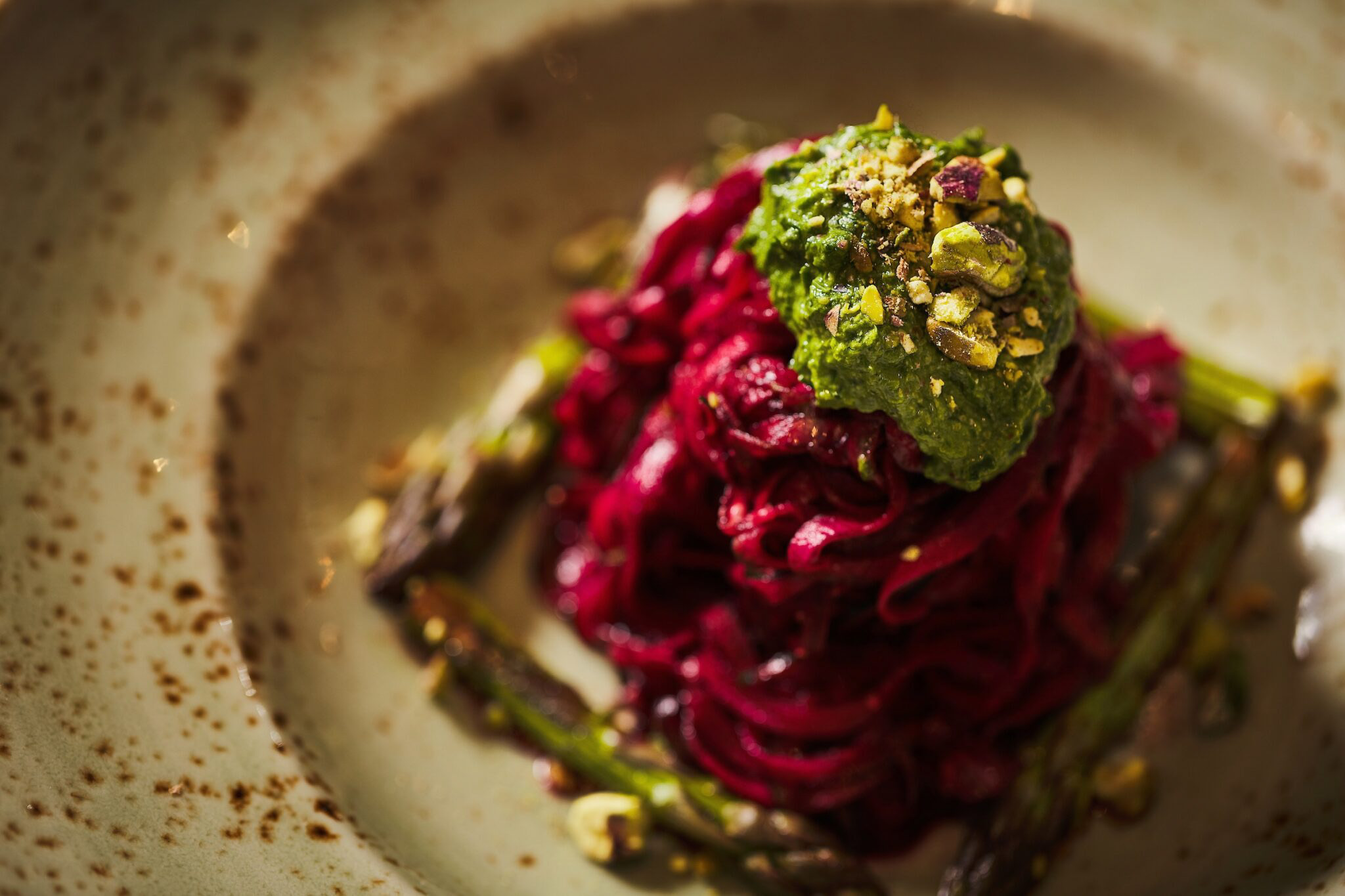 Beetroot spaghetti with vegan pesto on a rustic plate.