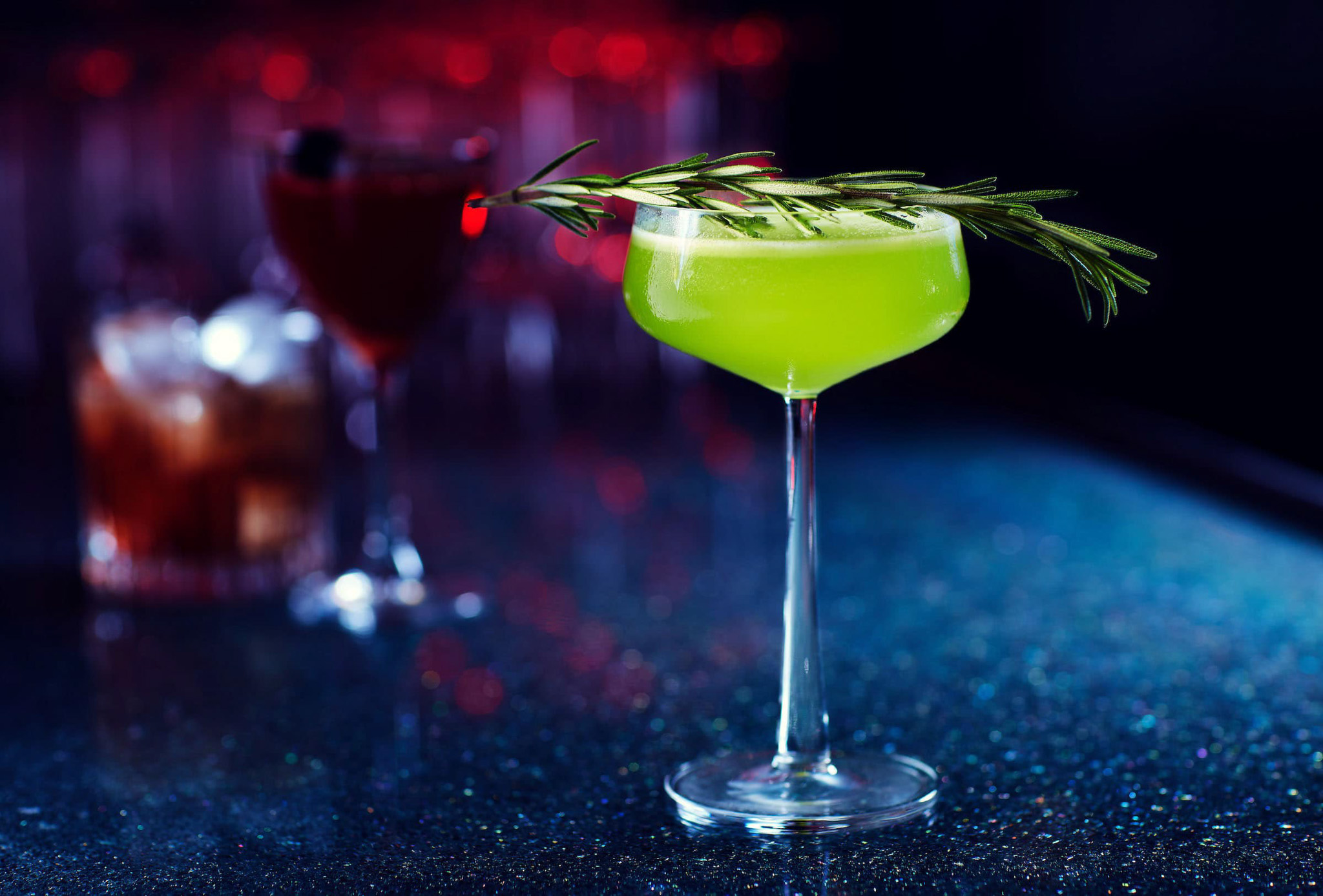 Vibrant green cocktail with rosemary on bar counter.