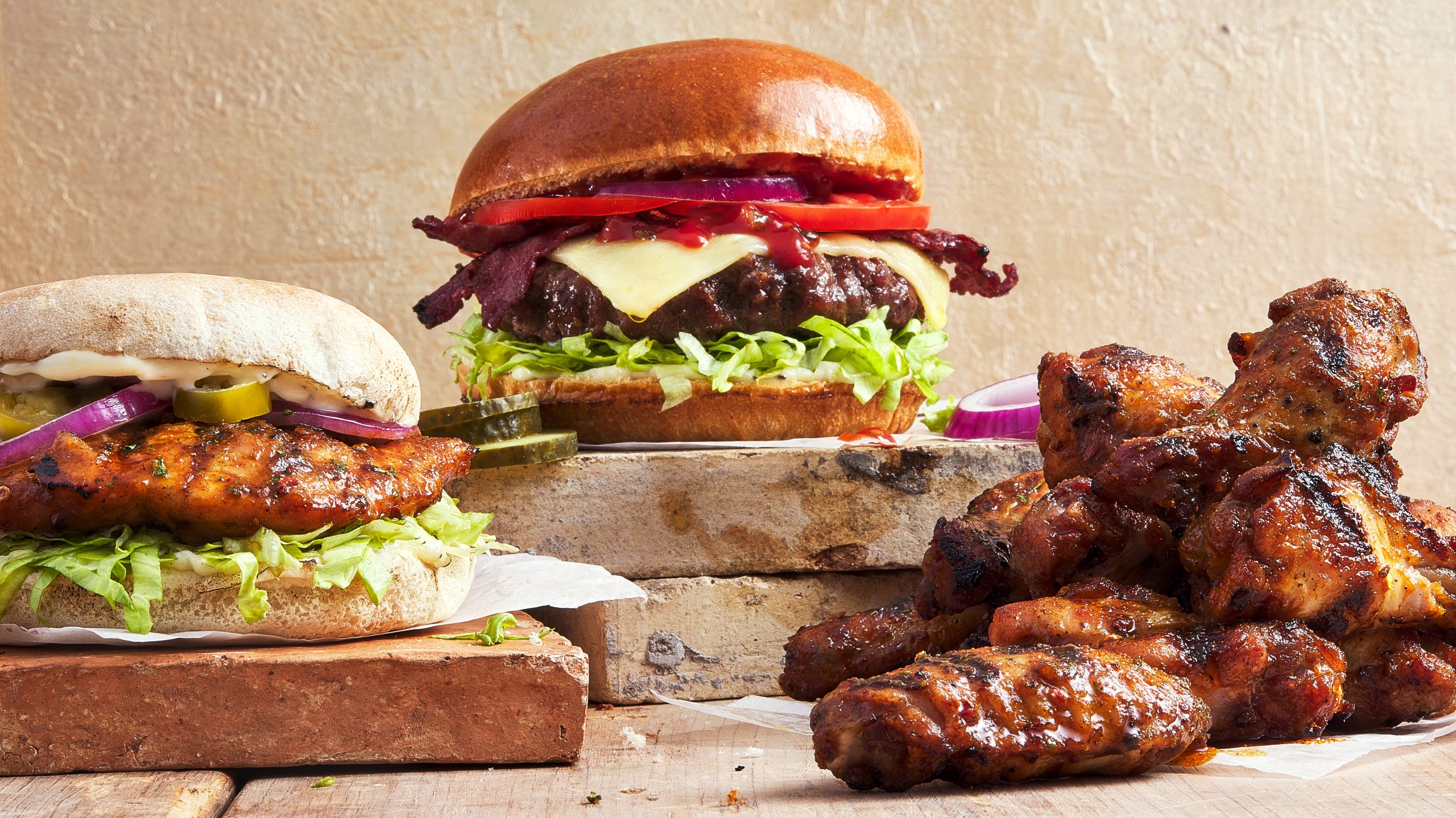Mouthwatering burgers and chicken wings on rustic background.