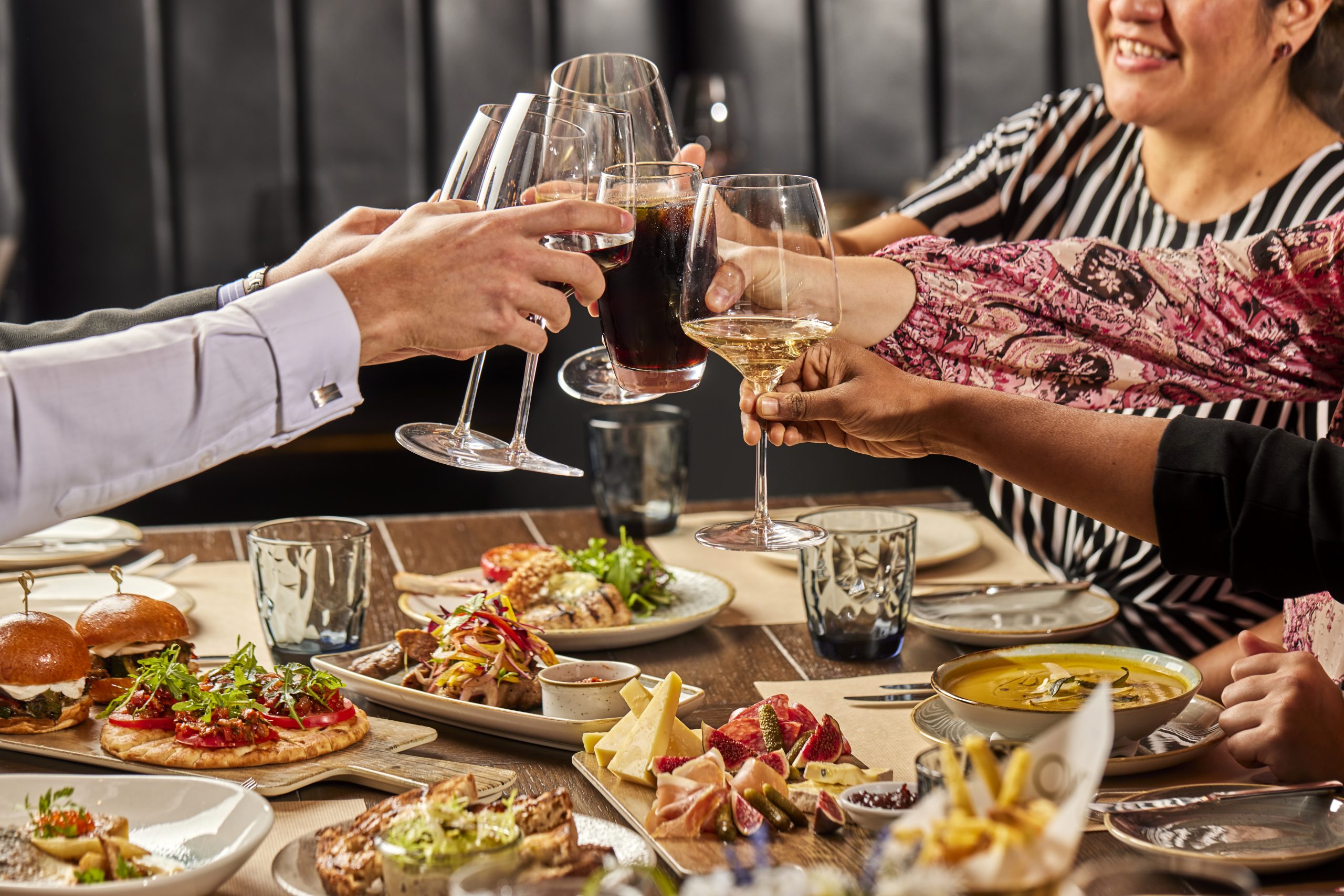 Friends celebrating with wine, gourmet food, and cheers at a festive dinner gathering.