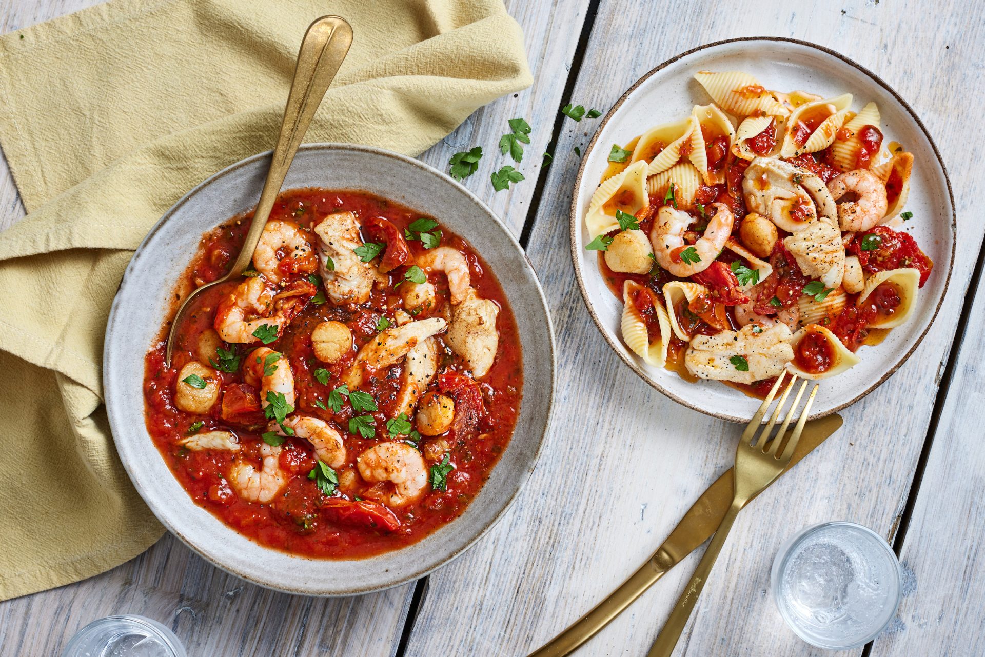 Seafood bowl with tomato broth and shell pasta on a rustic wooden table.