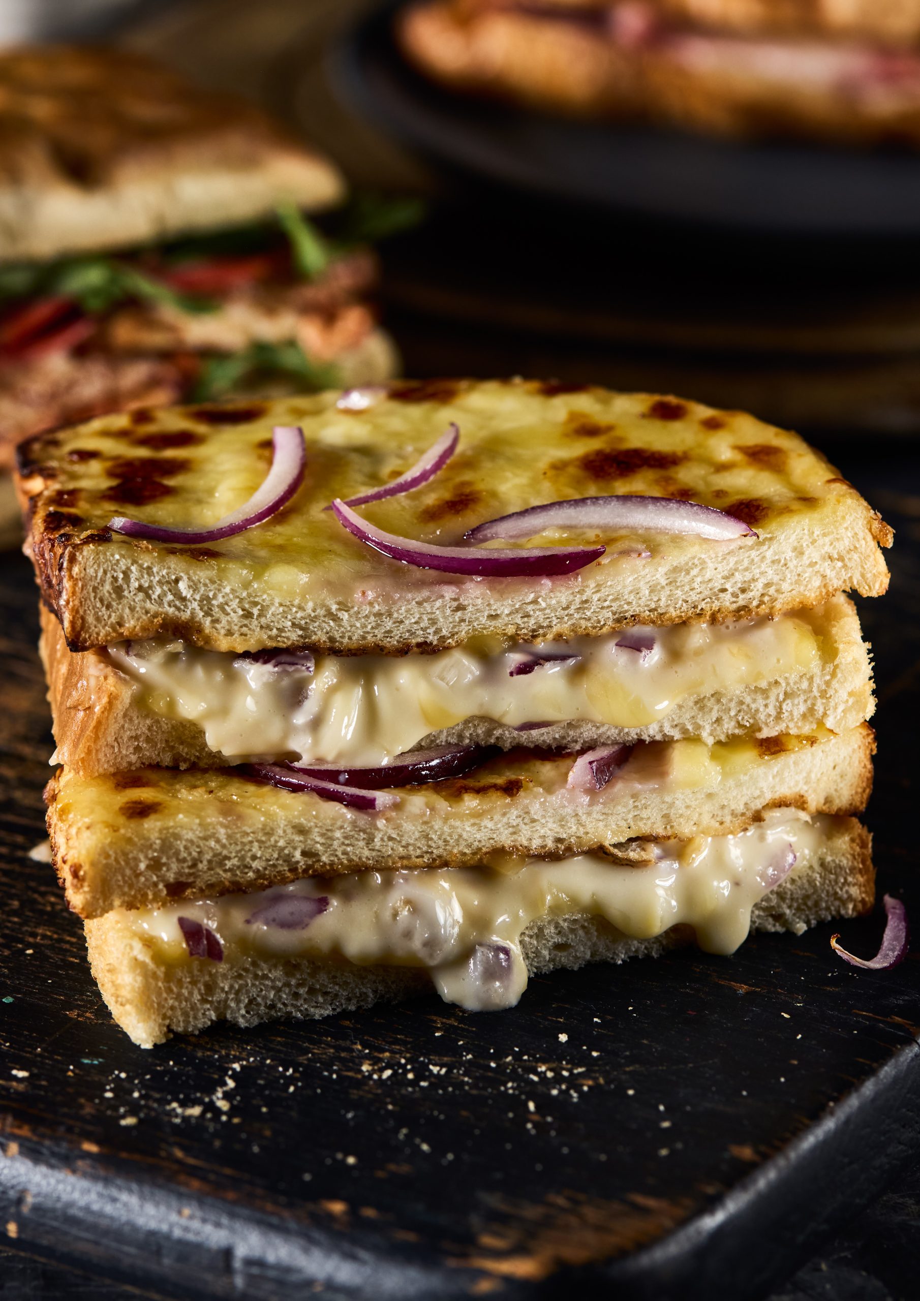Close-up of a crispy grilled cheese and red onion sandwich on rustic dark background.