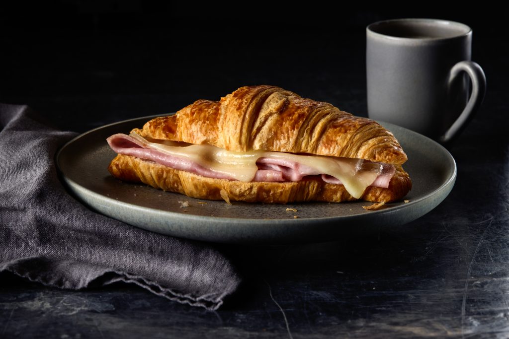 Golden ham and cheese croissant with coffee on grey plate, cosy minimalist breakfast setting.