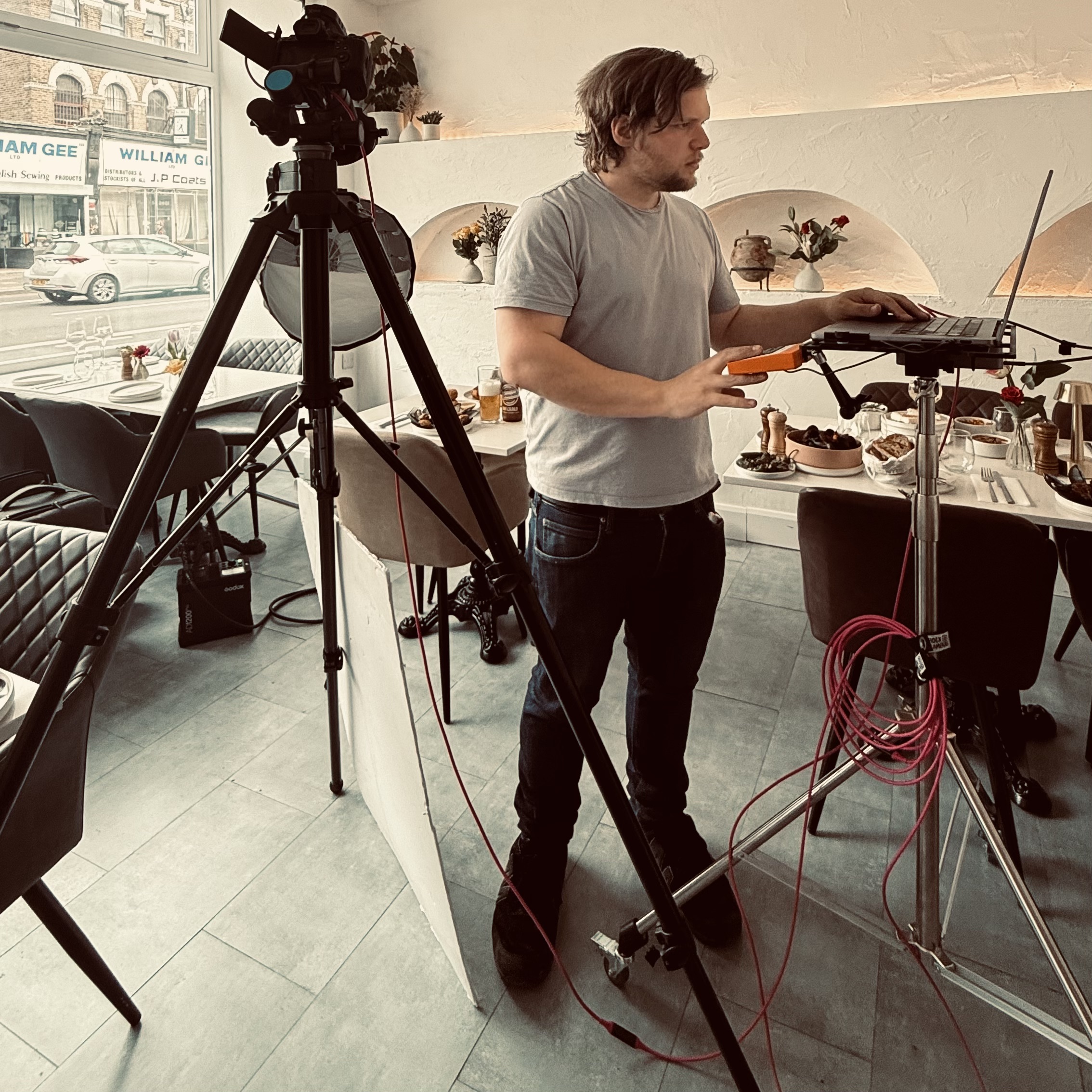 Man using laptop beside camera and lighting setup in a stylish urban café.