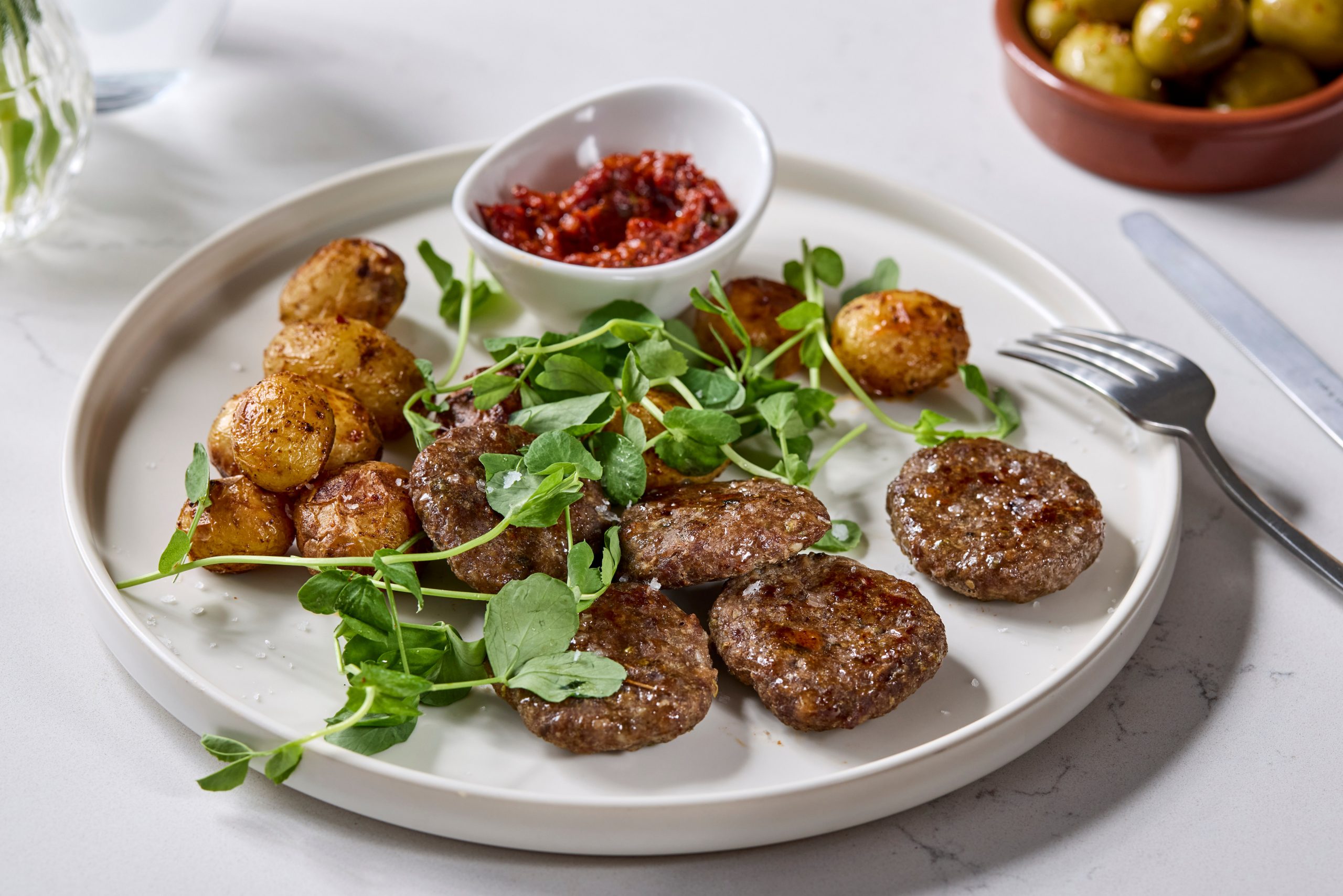 Seared meat patties with roast baby potatoes, pea shoots and red pepper relish